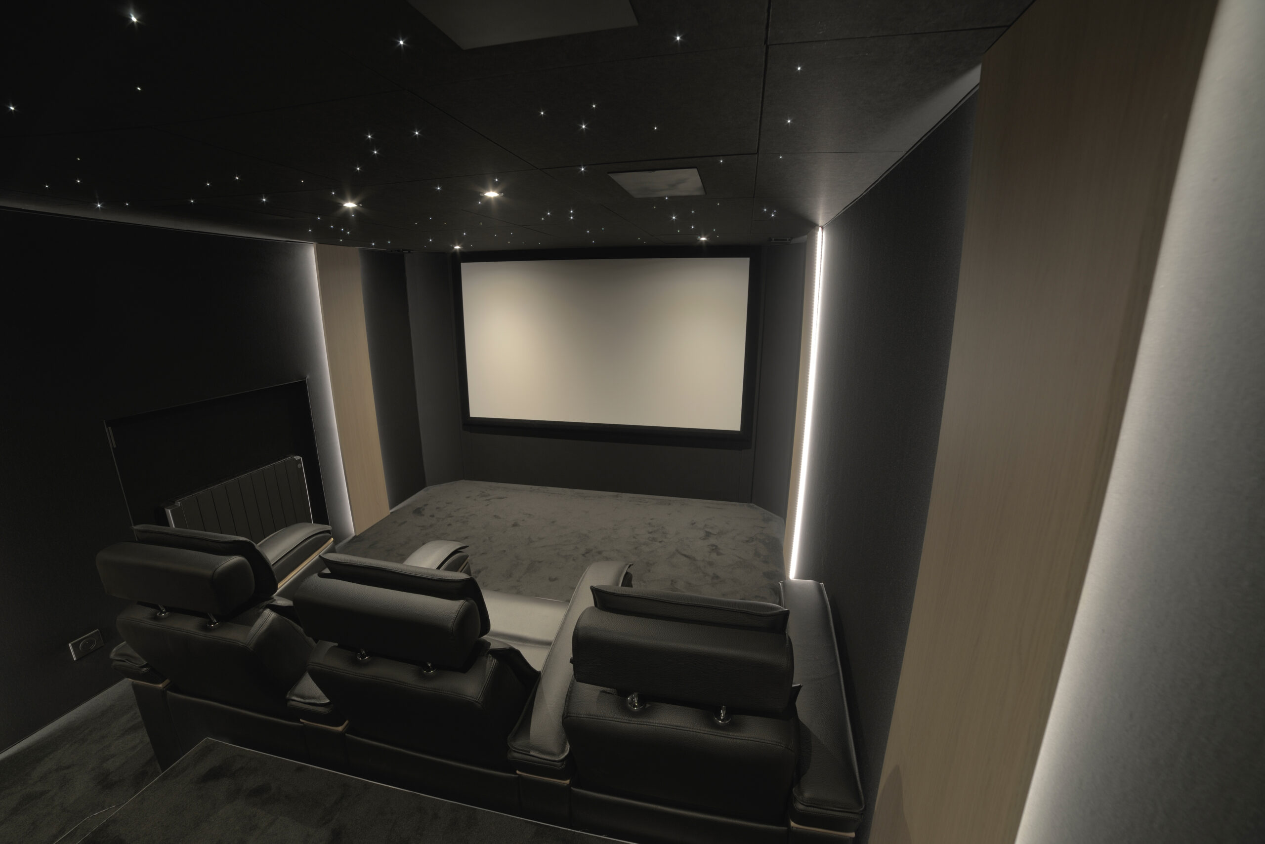 Salle de cinéma privée 17m2 avec 5 fauteuils en cuir noir, ciel étoilé, spots, panneaux décor chêne rétro-éclairés à Créteil