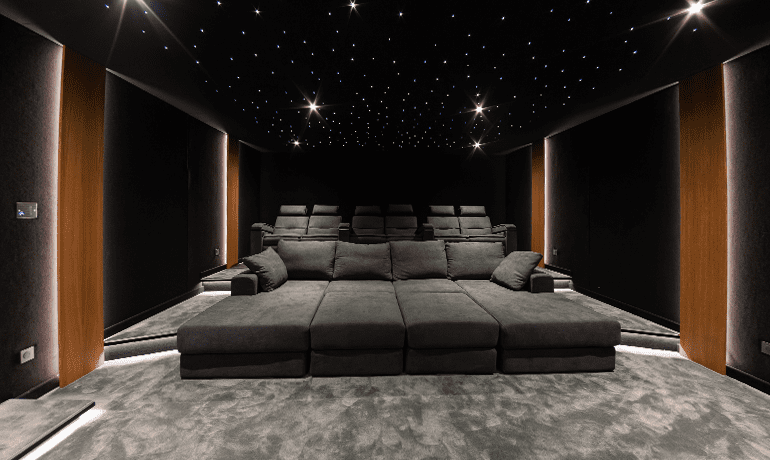 Salle de cinéma à la maison avec moquette douce grise, 10 sièges gris dont 4 places allongées, plafond étoilé de lumières blanches et murs en bois