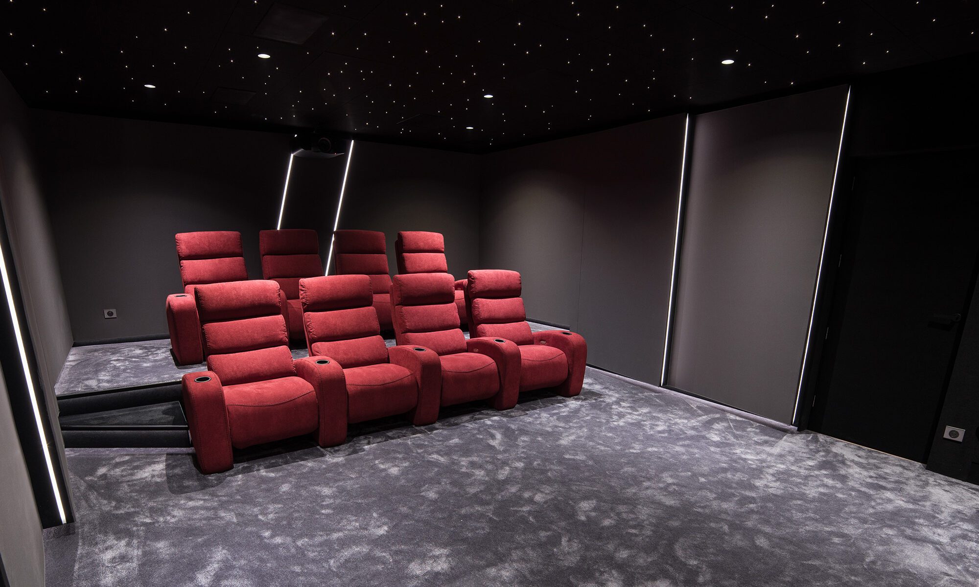 Salle de cinema privée 35m2 rouge 9 places, fauteuils en tissu rouge, tissu tendu gris anthraacite, avant-scène, ciel étoilé, spots, panneaux lumineux au Havre