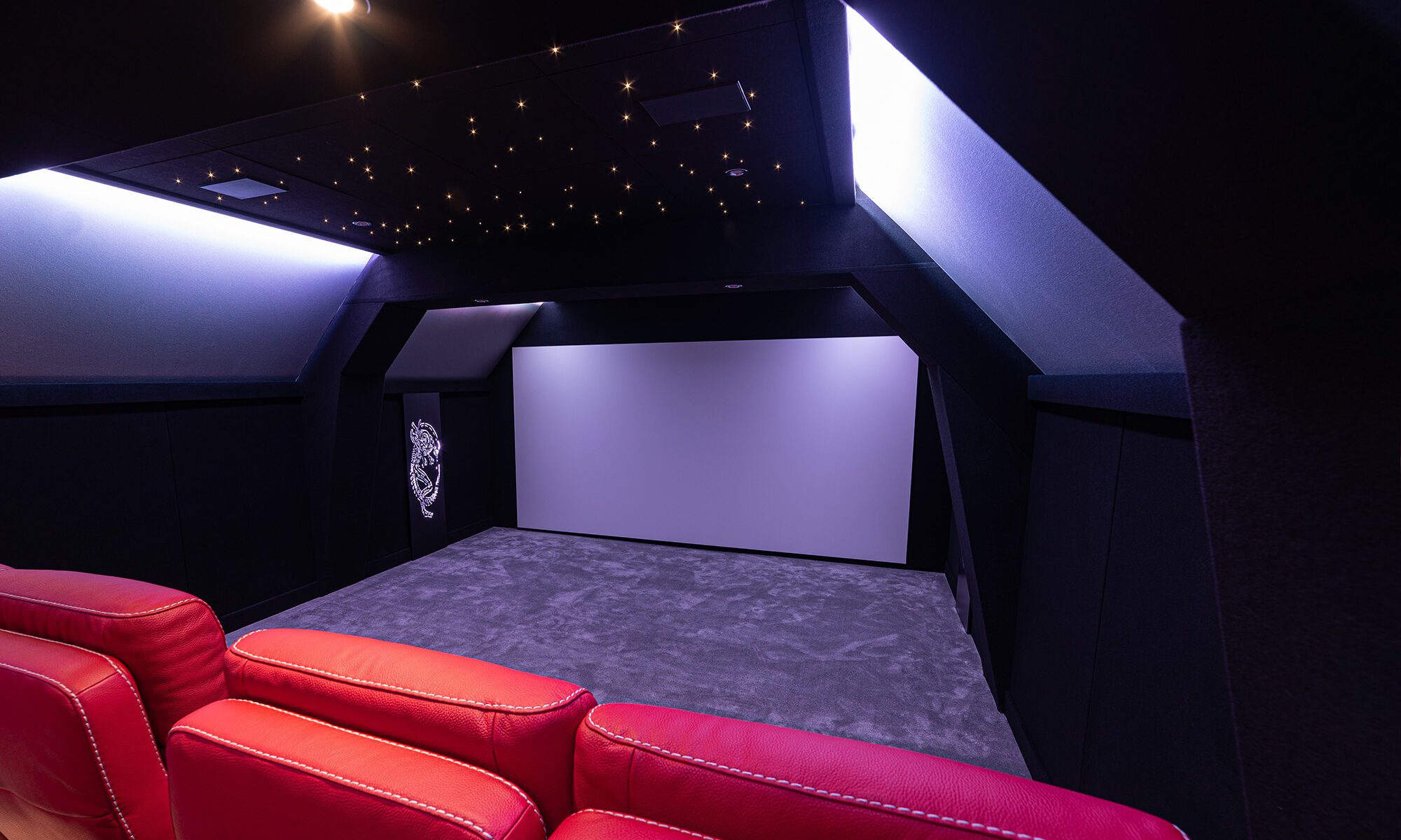 Salle de cinéma privée 8 places 39m2 avec fauteuils en cuir rouge, panneaux décor métalliques, corniche lumineuse, ciel étoilé et spots à Rouen