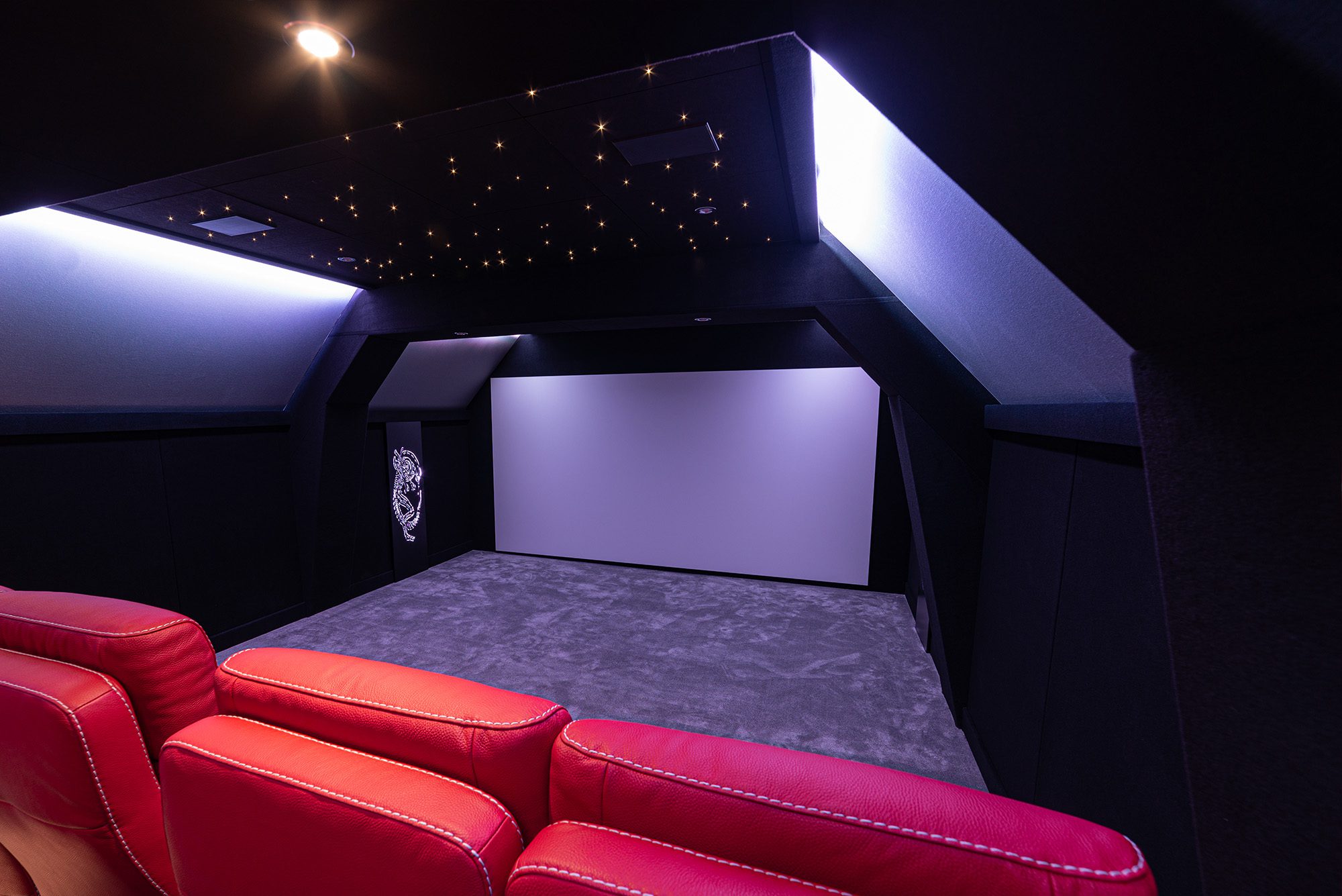 Salle de cinéma privée 8 places 39m2 avec fauteuils en cuir rouge, panneaux décor métalliques, corniche lumineuse, ciel étoilé et spots à Rouen