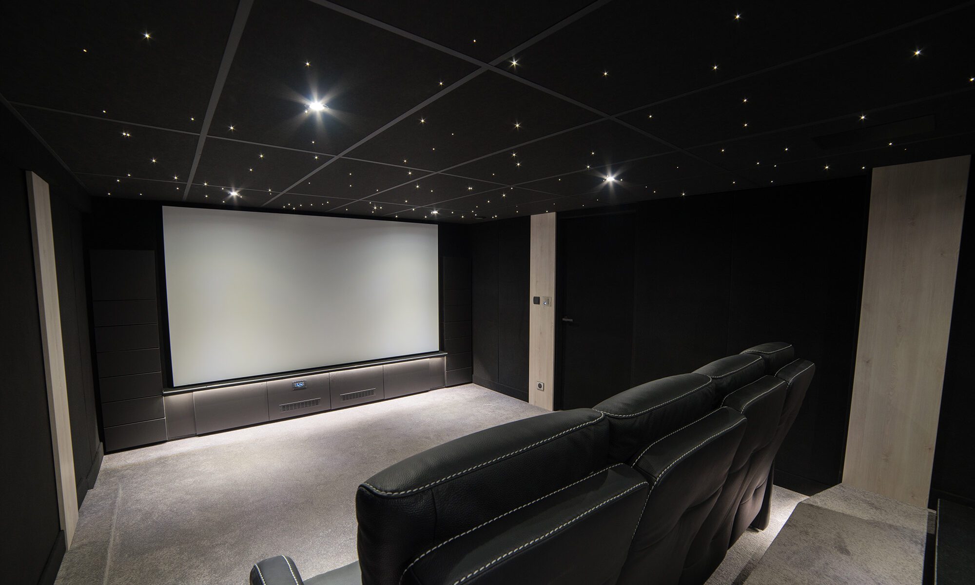 Salle de cinéma privée 26m2 avec 8 fauteuils en cuir et tissu noir, panneaux décor chêne, meuble technique sur-mesure sous l'écran à Evry