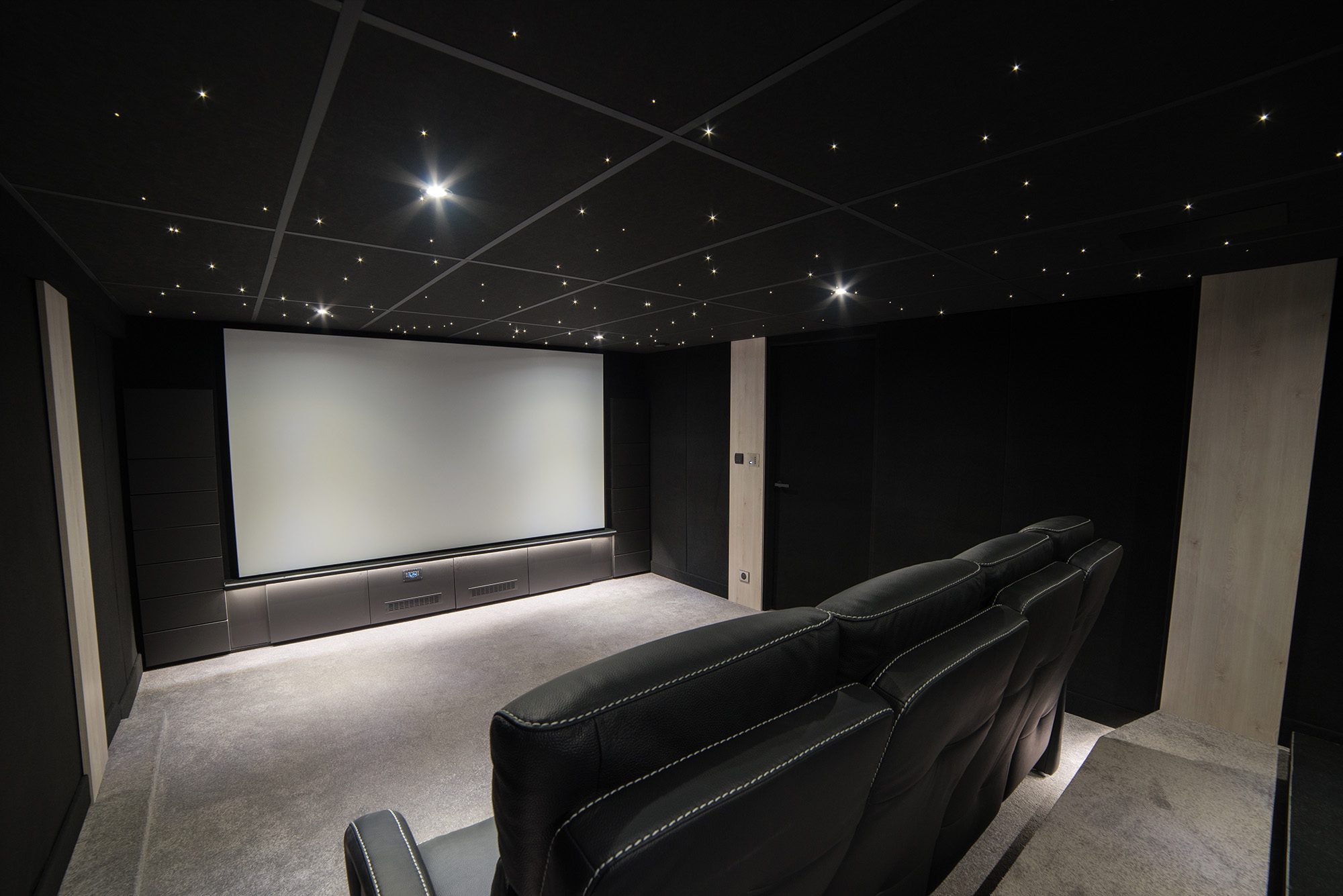 Salle de cinéma privée 26m2 avec 8 fauteuils en cuir et tissu noir, panneaux décor chêne, meuble technique sur-mesure sous l'écran à Evry