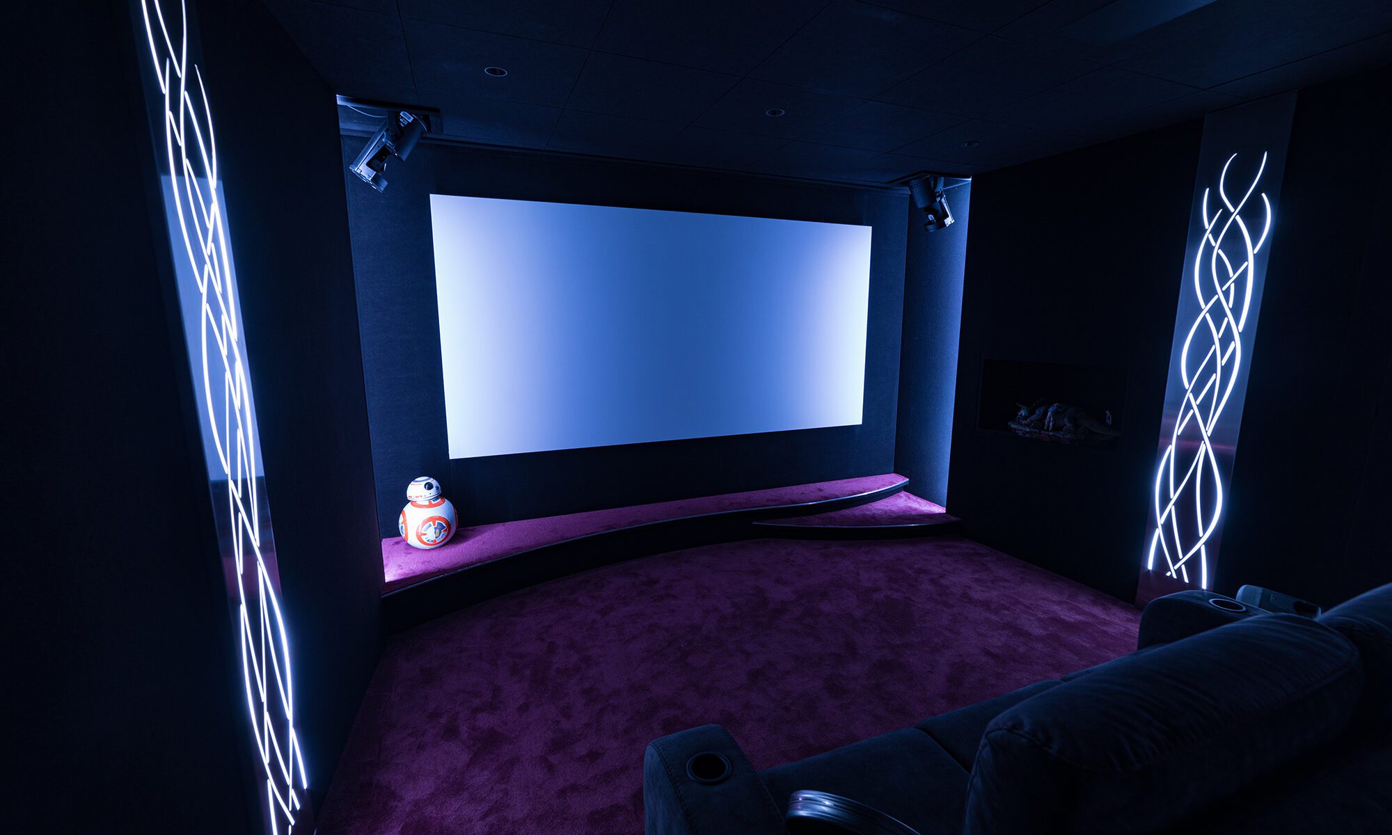 Salle de cinéma privée 24m2 avec 6 fauteuils en tissu gris foncé, avant-scène courbe, panneaux décor métalliques, niche lumineuse, jeux de lumières, ciel étoilé, spots, régie de disque jockey à Versailles