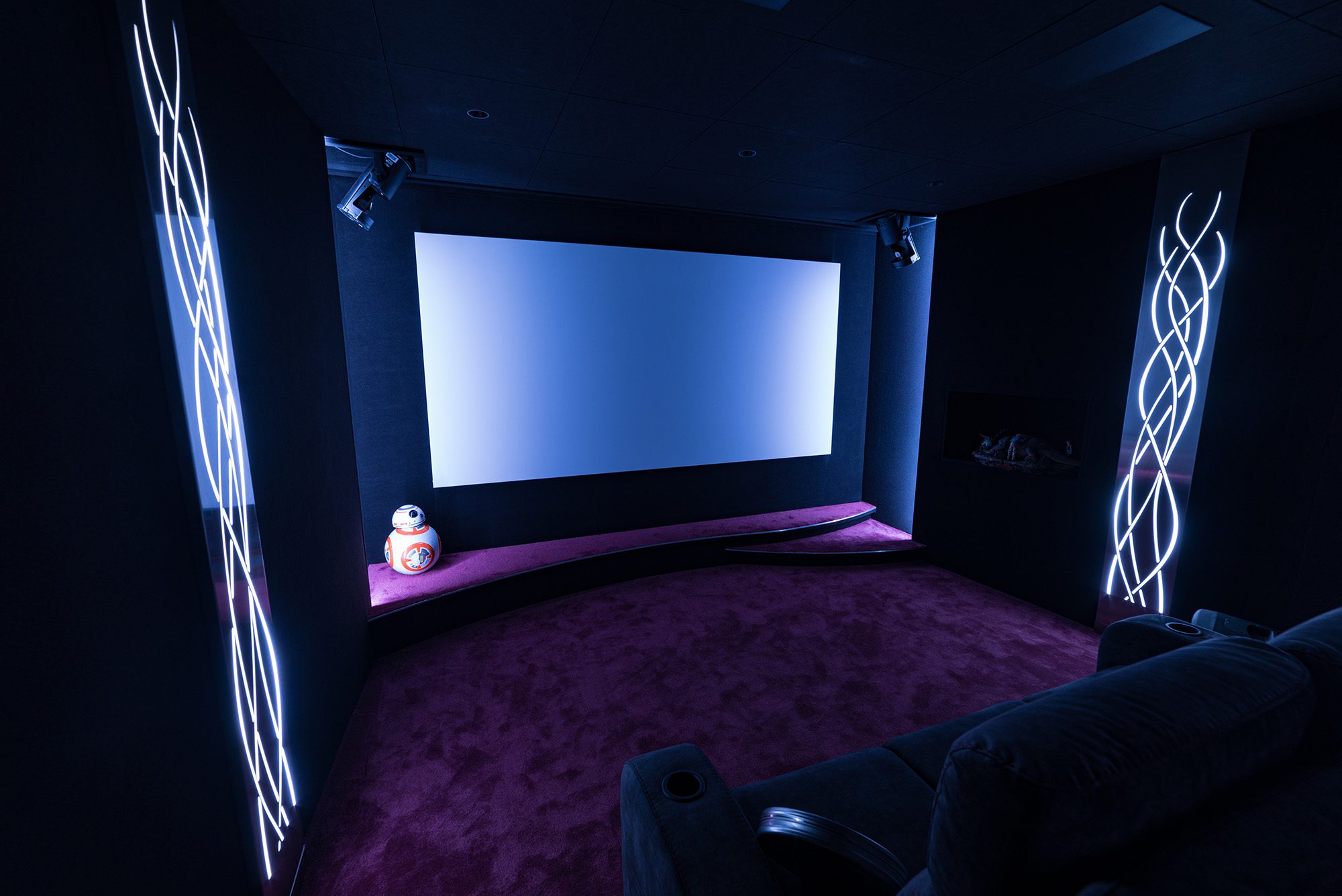 Salle de cinéma privée 24m2 avec 6 fauteuils en tissu gris foncé, avant-scène courbe, panneaux décor métalliques, niche lumineuse, jeux de lumières, ciel étoilé, spots, régie de disque jockey à Versailles