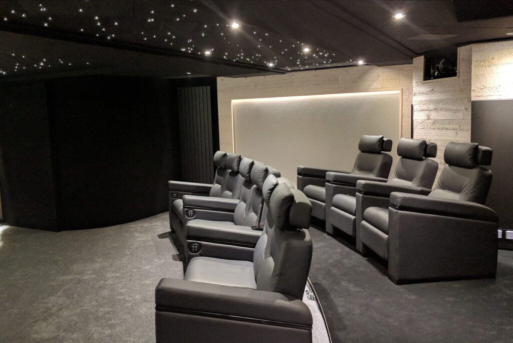 Salle de cinéma privée 76m2 avec 9 fauteuils en cuir noir, panneaux chêne, meubles et bar sur-mesure, parquet et tissu tendu gris anthracite, ciel étoilé, spots et rubans led à Mageve