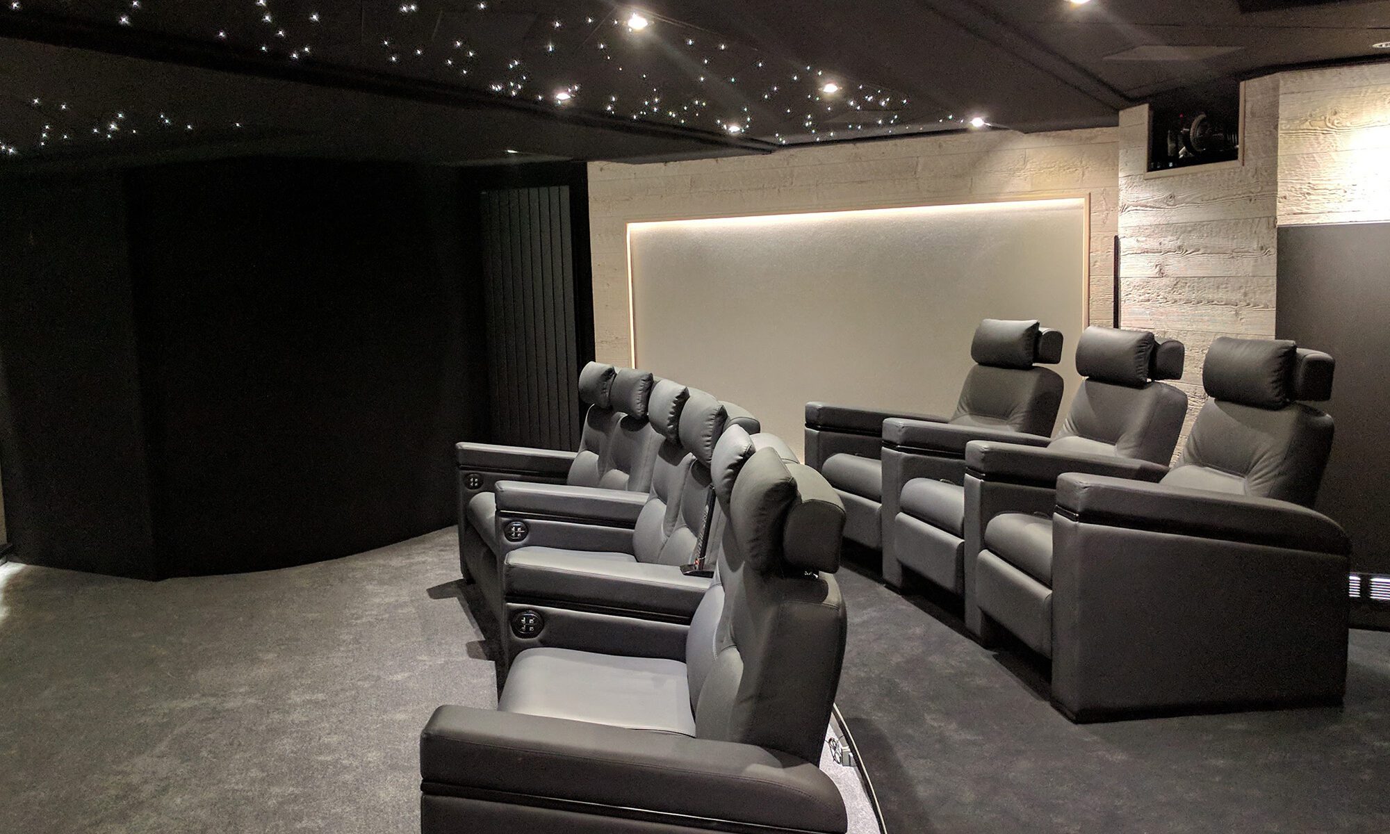 Salle de cinéma privée 76m2 avec 9 fauteuils en cuir noir, panneaux chêne, meubles et bar sur-mesure, parquet et tissu tendu gris anthracite, ciel étoilé, spots et rubans led à Mageve