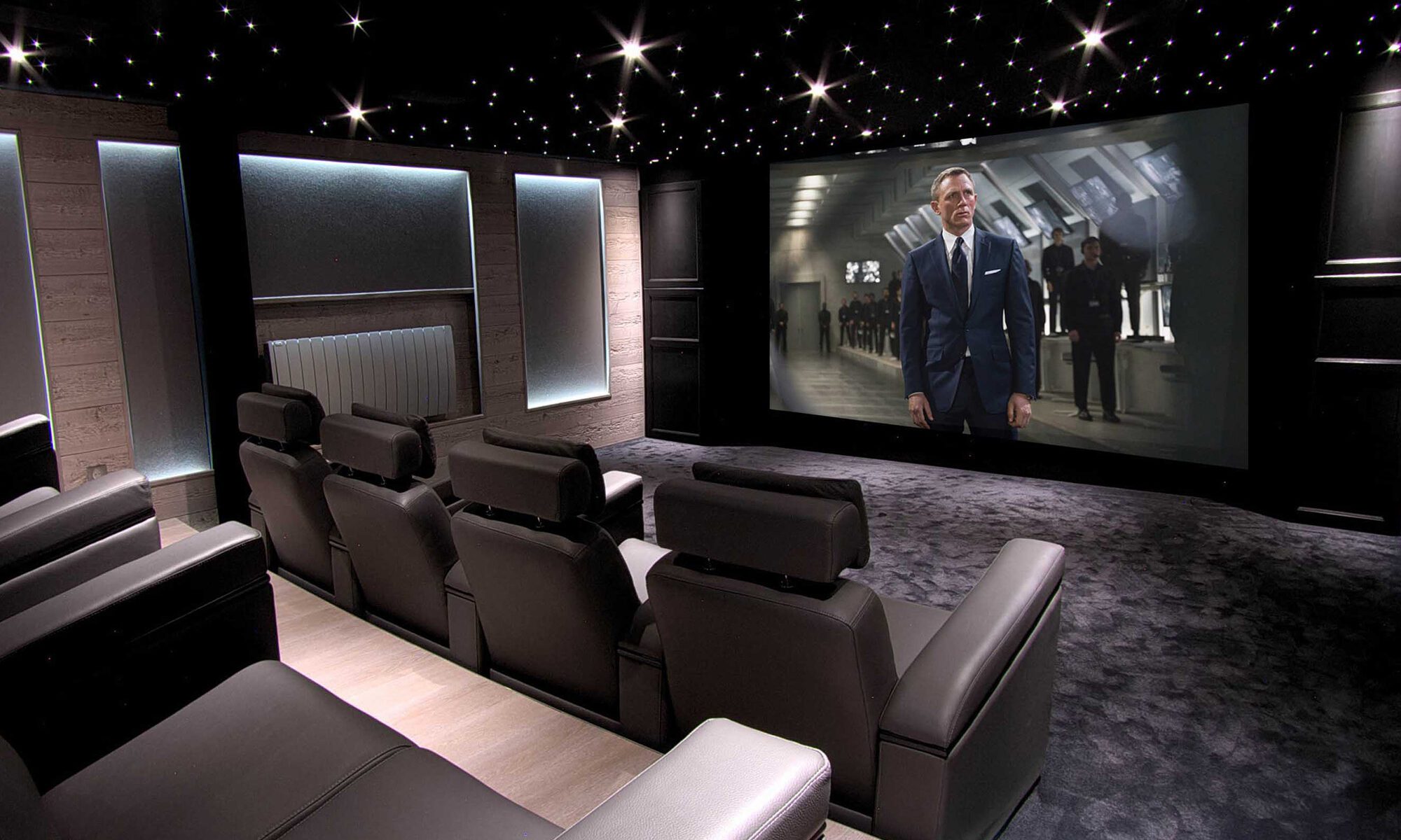 Salle de cinéma privée 50m2 avec 9 fauteuils en cuir noir, panneaux chêne, meubles et bar sur-mesure, parquet et tissu tendu gris anthracite, ciel étoilé, spots et rubans led à Mageve