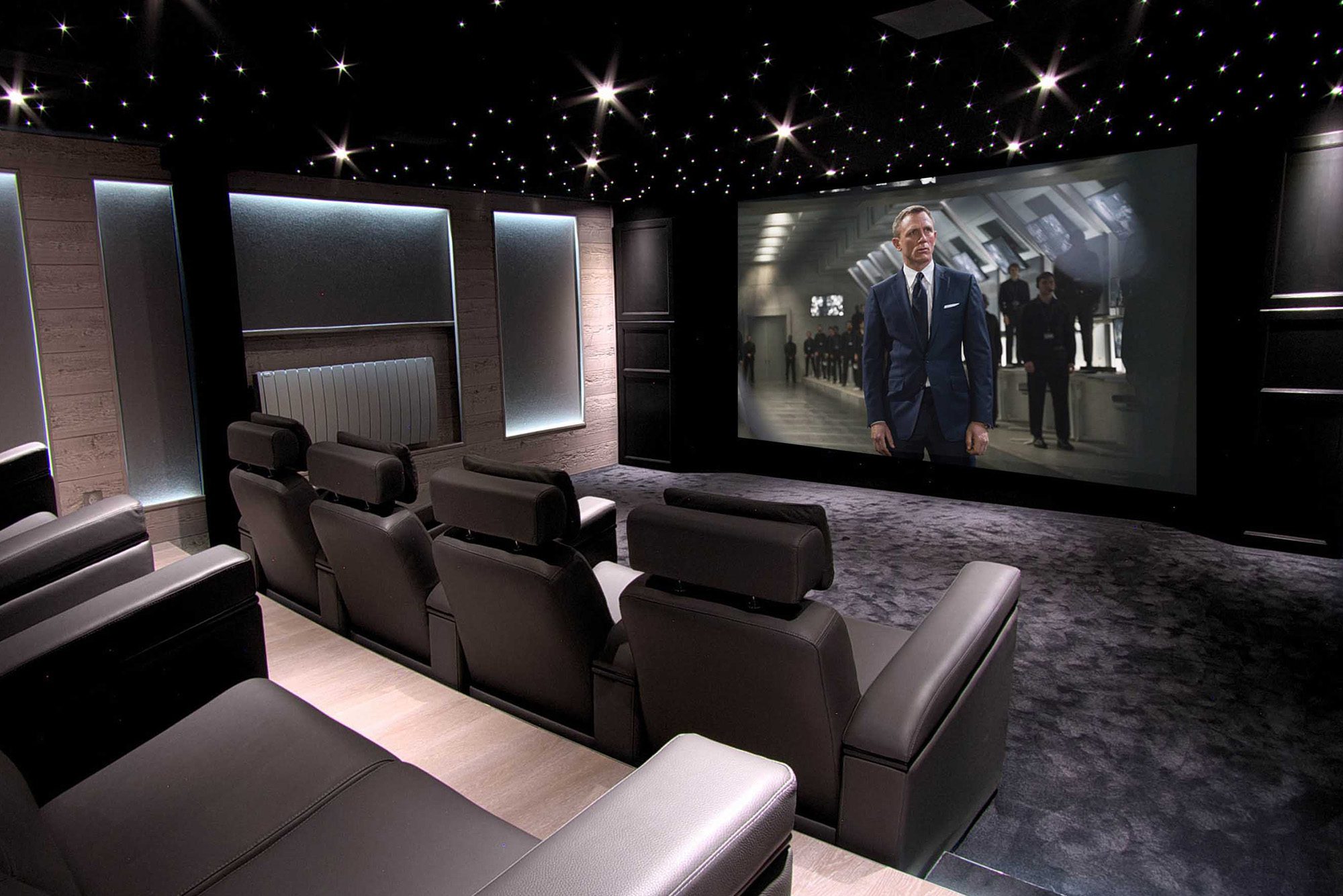 Salle de cinéma privée 50m2 avec 9 fauteuils en cuir noir, panneaux chêne, meubles et bar sur-mesure, parquet et tissu tendu gris anthracite, ciel étoilé, spots et rubans led à Mageve