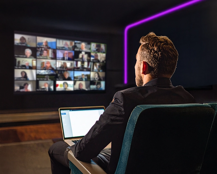 Homme télétravaillant dans sa salle de cinéma privée. Il est assit devant son écran HD en vidéo conférence avec des collaborateurs.