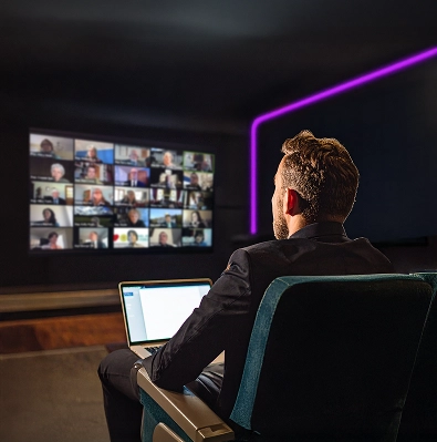 Man die telewerkt in zijn privébioscoopzaal. Hij zit voor zijn HD-scherm in een videoconferentie met medewerkers.