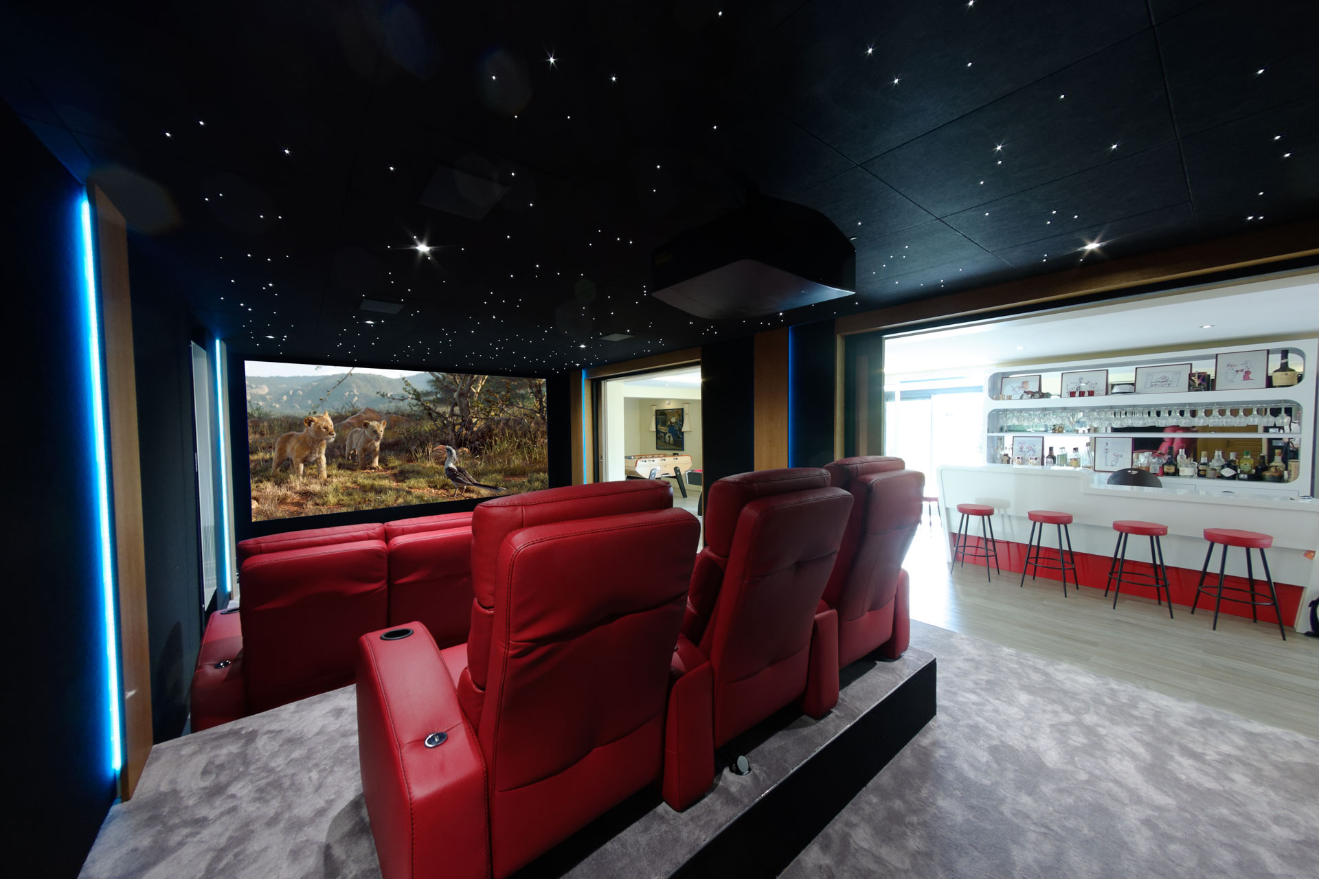 Deux rangées de fauteuils relax rouges face à un écran de cinéma avec bar ouvert à l’arrière