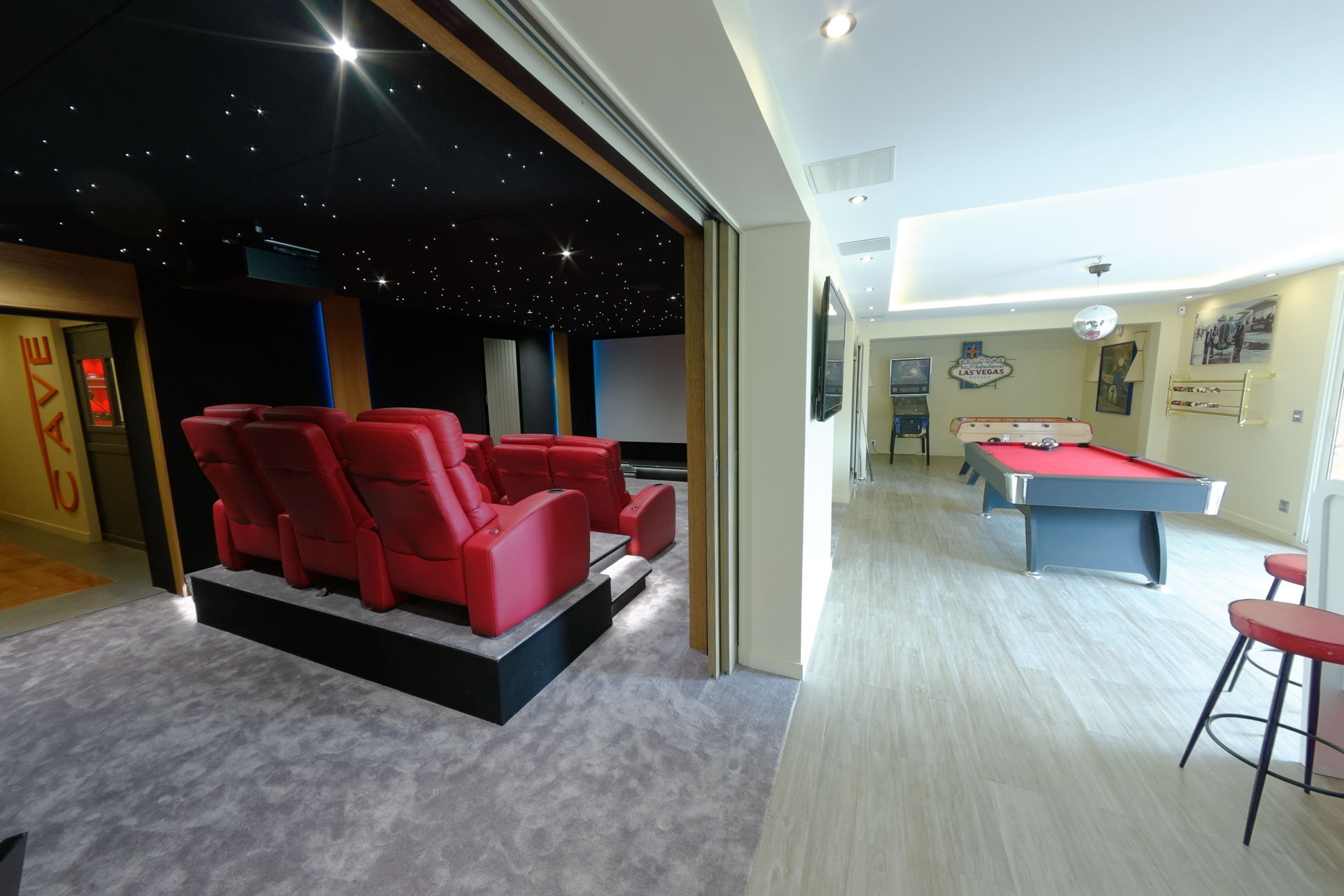 Salle cinéma avec fauteuils rouges ouverte sur un billard, un baby-foot, un flipper et un bar