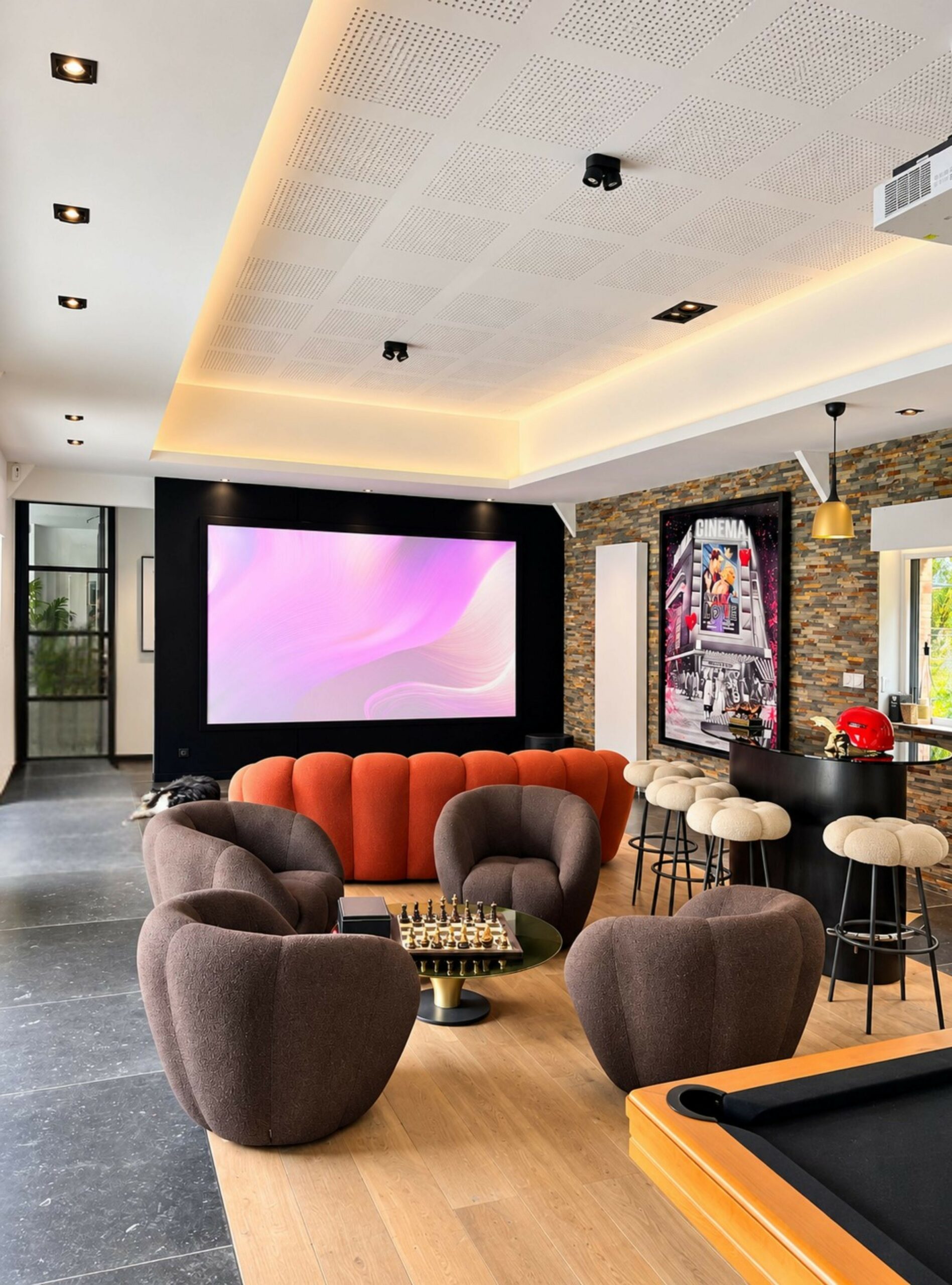 Billard au premier plan face à un écran de projection et un salon dans un espace de loisirs