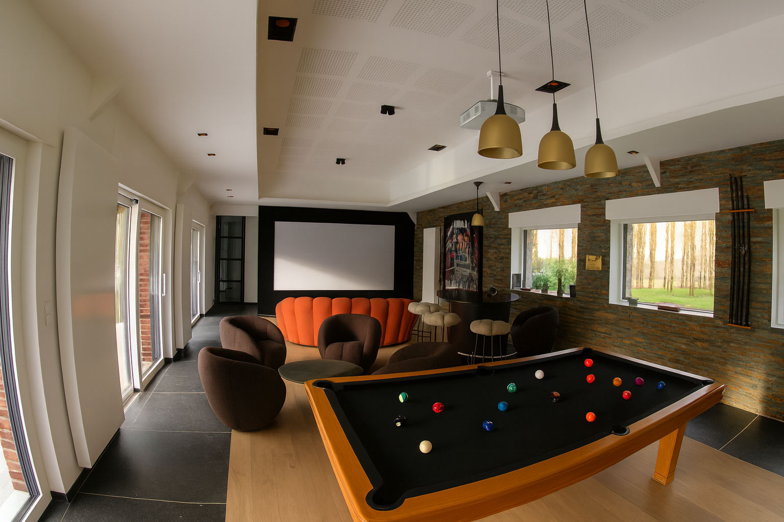 Espace de loisirs à Lille avec écran de 3 m, canapé orange, fauteuils et bar